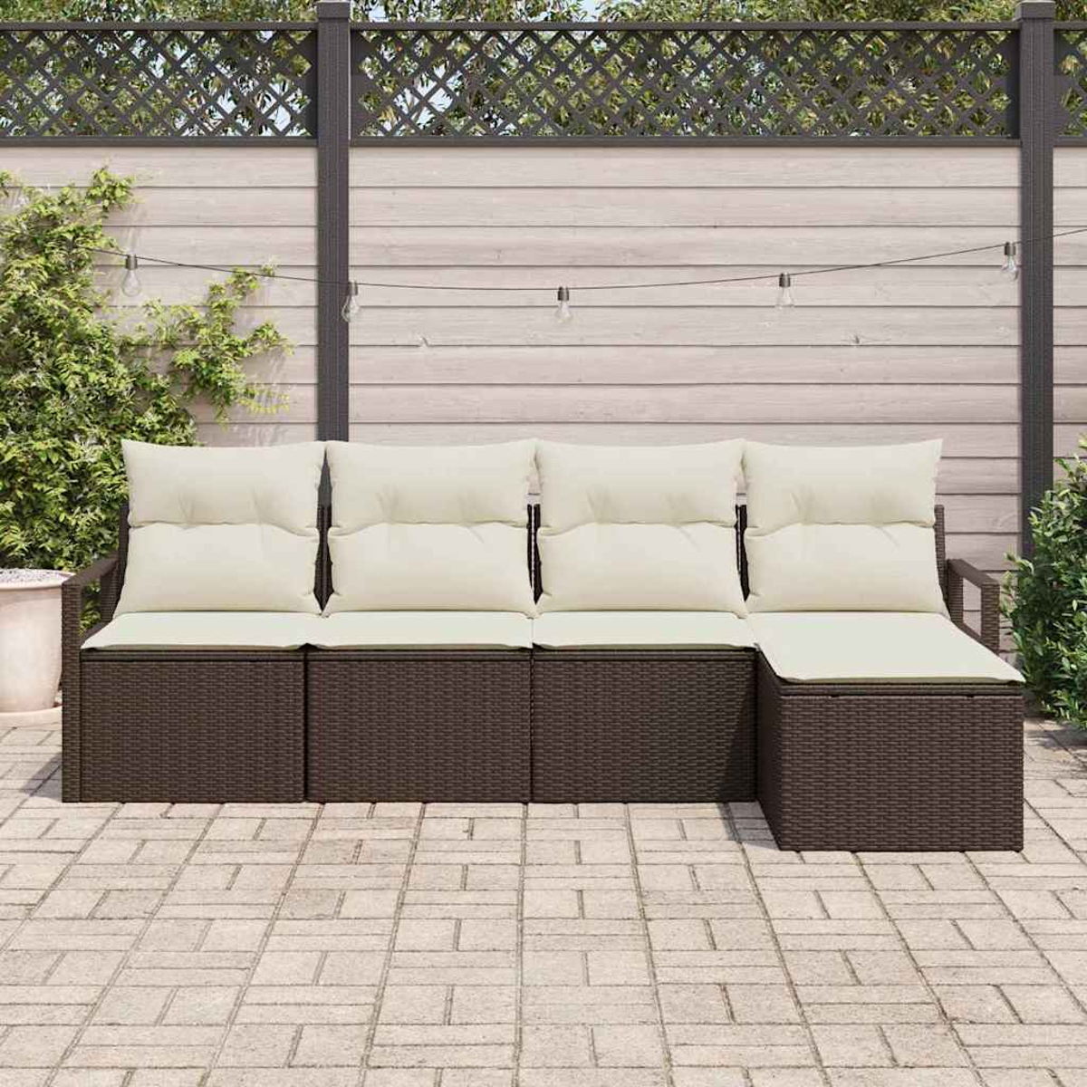 Outdoor-Ecksofa mit cremefarbenen Kissen. Brauner gewebter Sockel. Hintergrund: Zaun, Pflanzen und Lichterketten auf einer Terrasse.