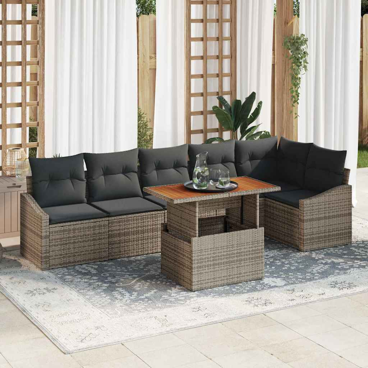 Outdoor-Korbmöbel-Set mit grauen Kissen auf einem gemusterten Teppich. Enthält einen Tisch mit Gläsern und weiße Vorhänge.