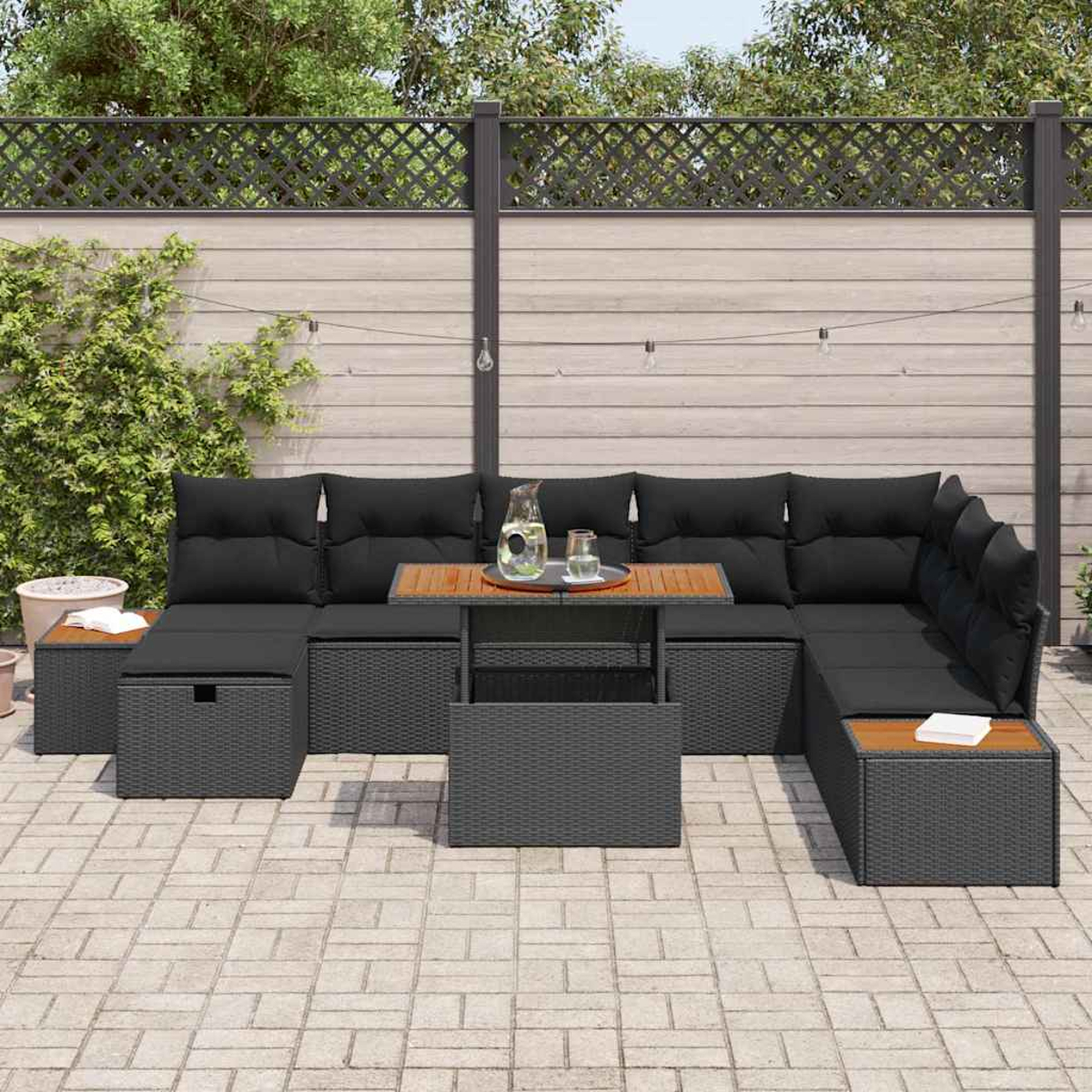 Outdoor-Ecksofa mit schwarzen Kissen und einem Holztisch. Im Hintergrund ein Zaun und Grün.