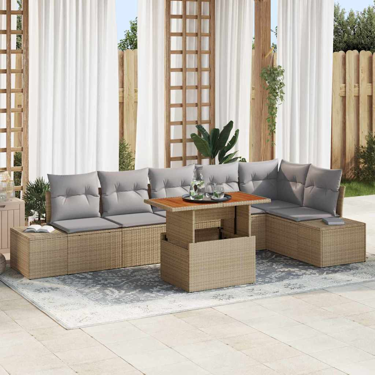 Zona de estar al aire libre con sofá y mesa de mimbre. Cojines grises y una alfombra. Cortinas blancas y valla de madera al fondo.
