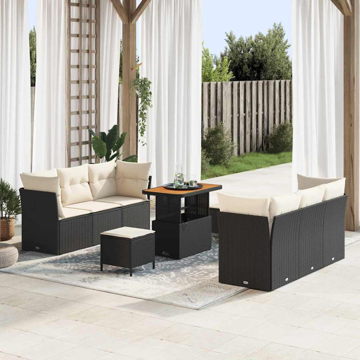 Juego de patio al aire libre. Sofá y sillas de mimbre negro con cojines beige. Una mesa pequeña y un otomán sobre una alfombra estampada.
