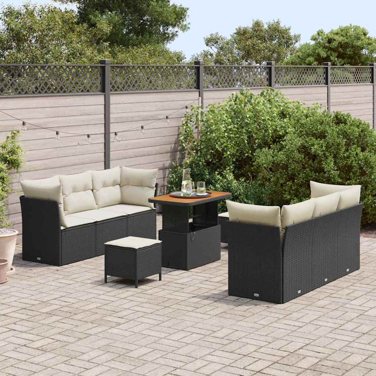 Conjunto de patio exterior con muebles de mimbre negro, cojines beige y mesa de madera. Fondo muestra valla y vegetación.