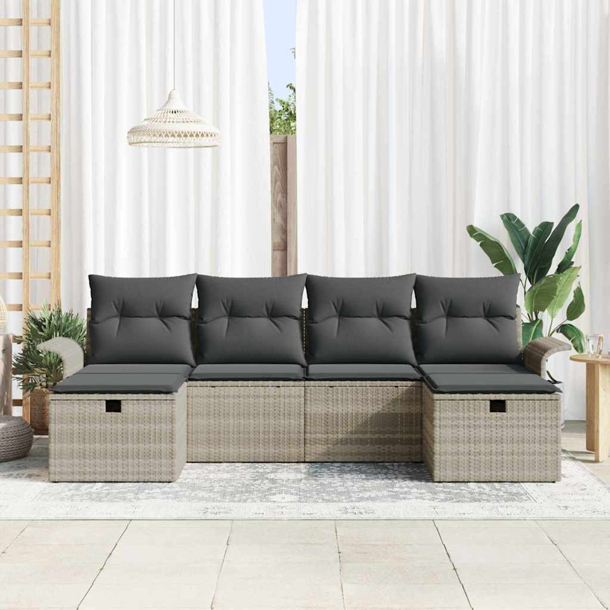 Outdoor-Sitzgruppe mit grauen Kissen und Rattan-Gestell. Weiße Vorhänge im Hintergrund. Pflanzen und eine Hängelampe ergänzen die Szene.