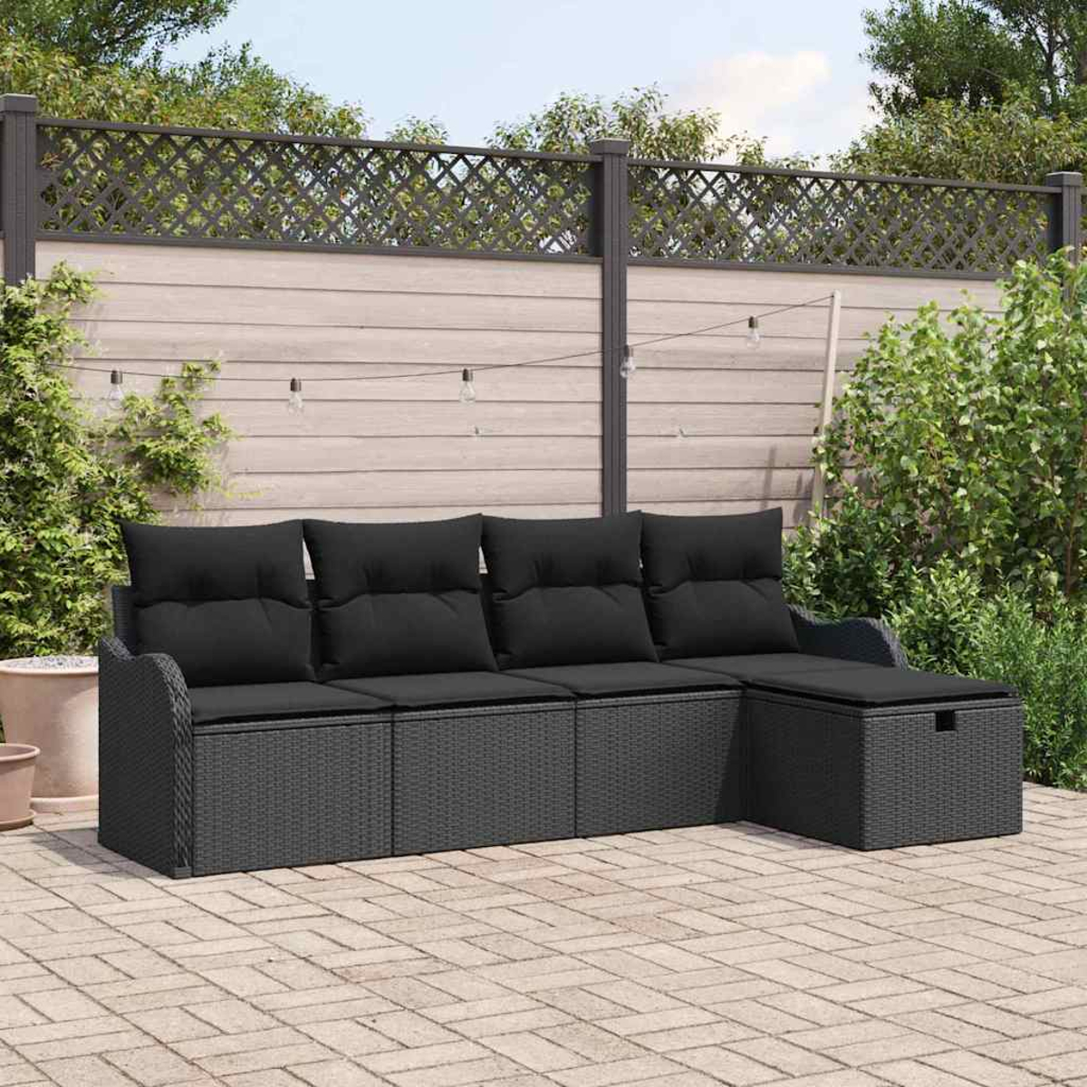 Dunkelgraues Rattan-Sofa mit schwarzen Kissen auf einer Ziegelterrasse. Dahinter ein Holzzaun mit Grün.