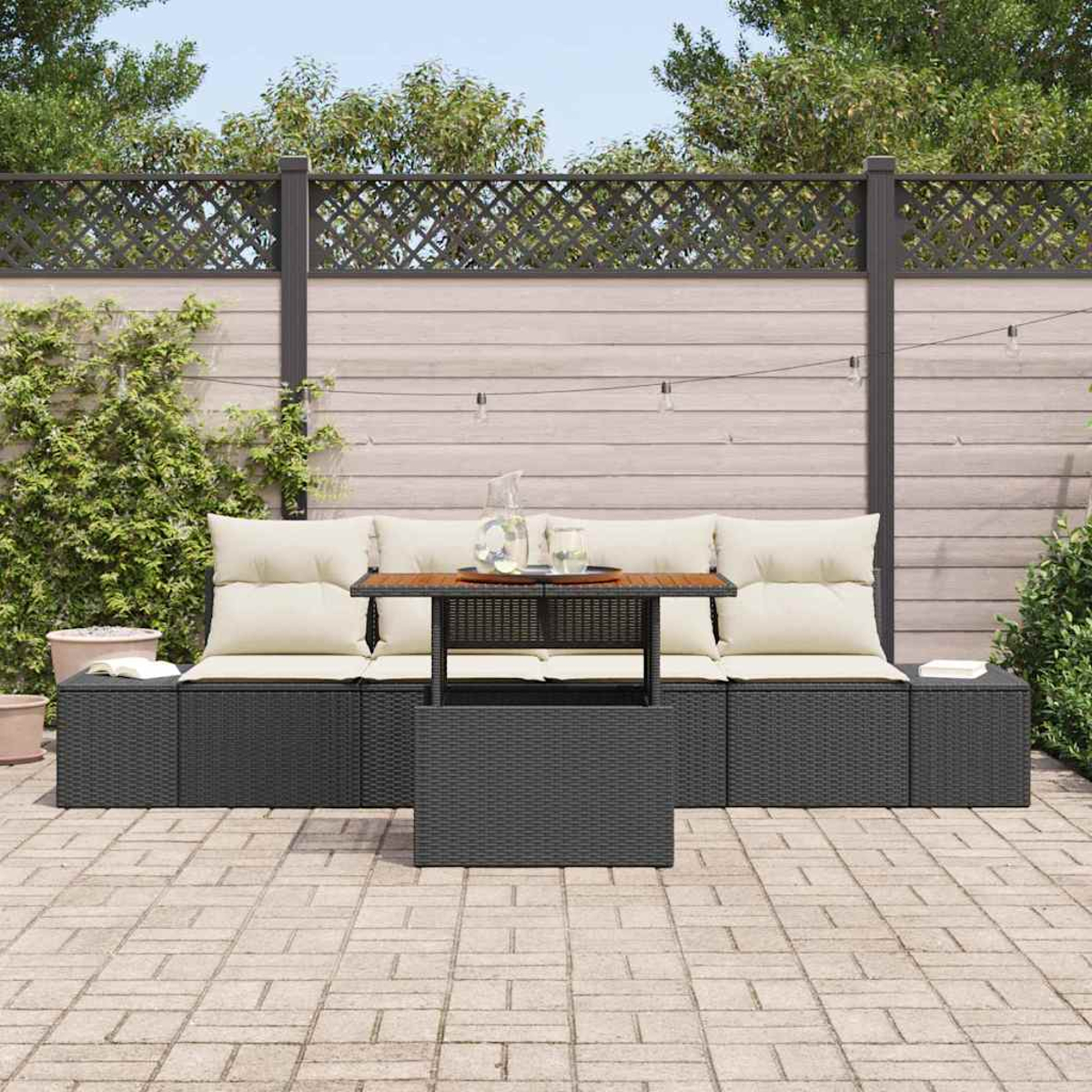 Garten-Set mit schwarzem Korbsessel, Holztisch und cremefarbenen Kissen. Im Hintergrund ein Zaun und Grün.