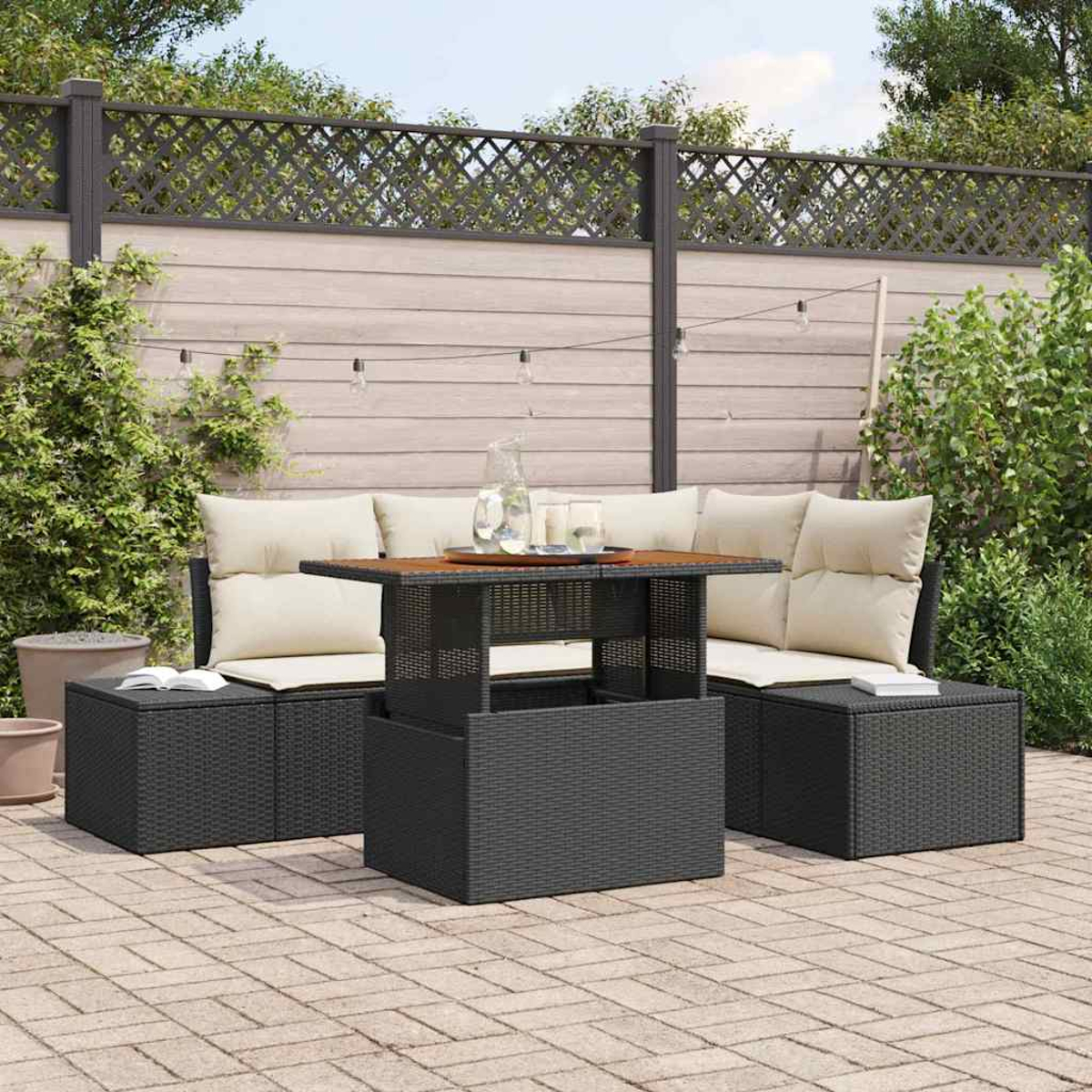 Juego de patio al aire libre con mesa y asientos. El juego es de mimbre gris oscuro con cojines beige claro. Una valla de madera en el fondo.