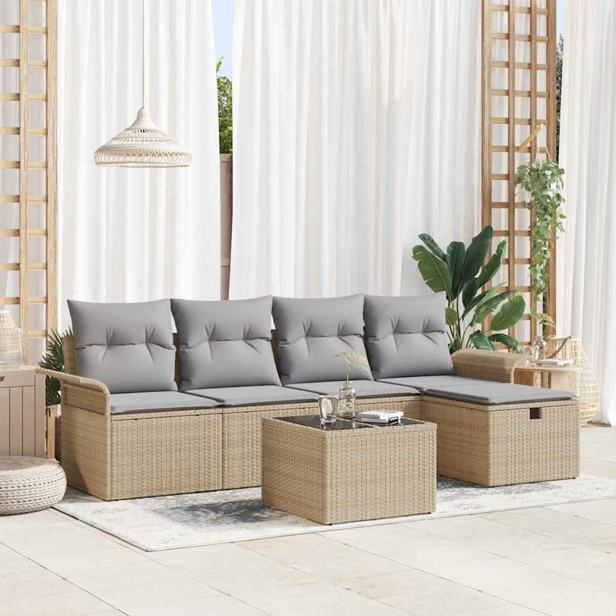 Außenbereich mit einem Korbmöbel-Sofa, Couchtisch und Hocker. Graue Kissen, weiße Vorhänge und Pflanzen sind sichtbar.