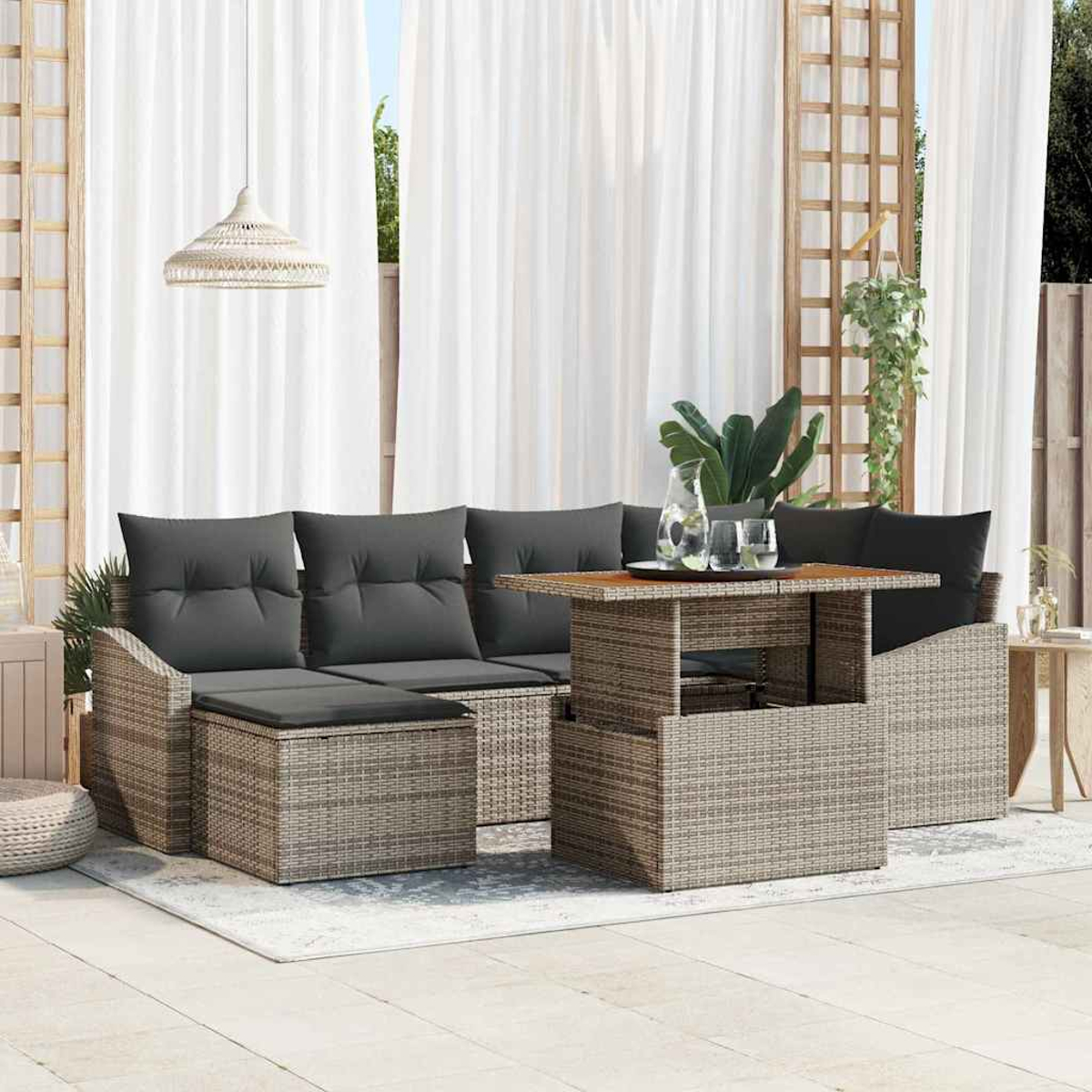Terrassengarnitur im Freien: graue Kissen, Korbmöbel, Holztisch, weiße Vorhänge und eine Hängelampe. Pflanzen und Gläser stehen auf dem Tisch.