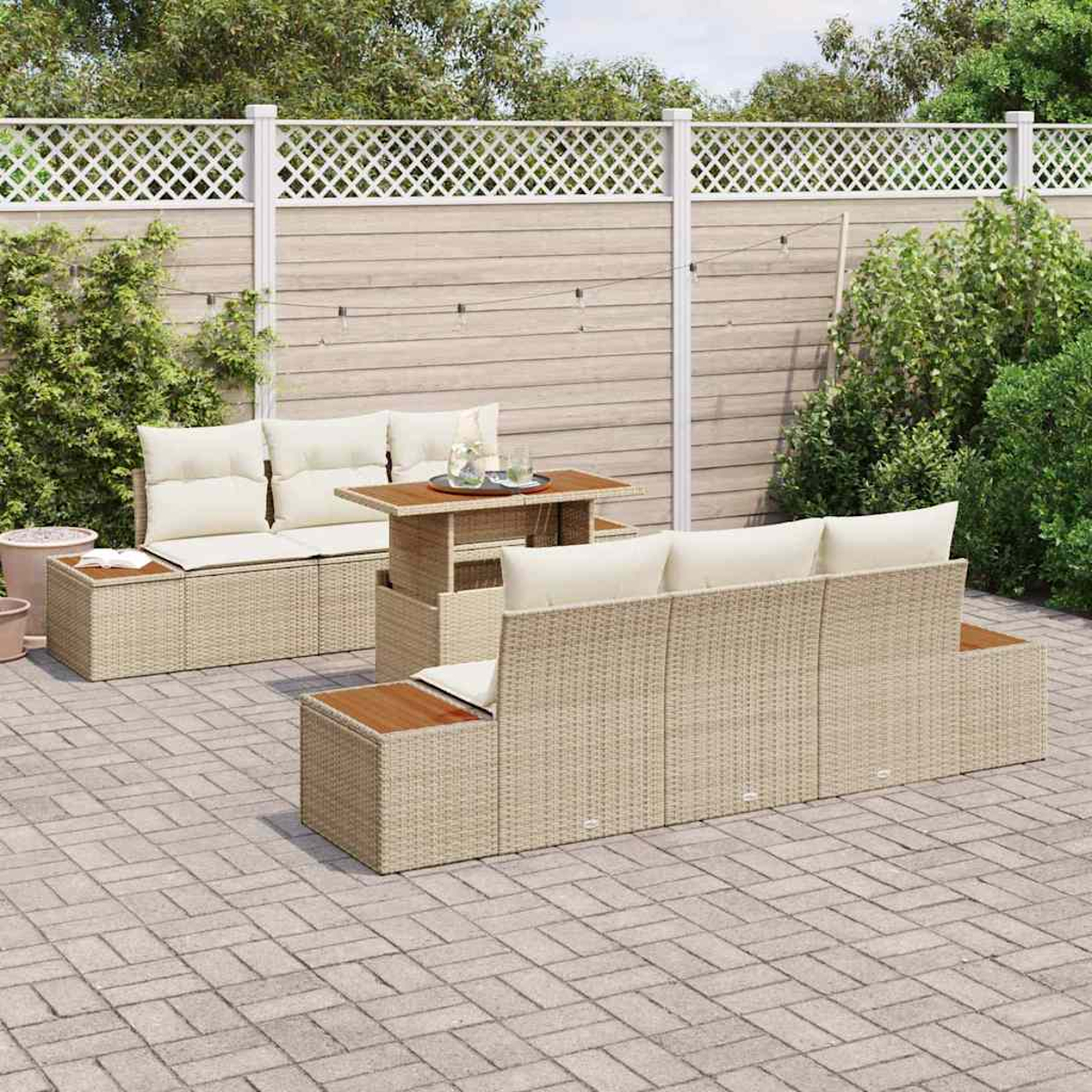 Gartenmöbel-Set. Beige Sofas und Tisch aus Korbgeflecht mit cremefarbenen Kissen. Auf einer Backstein-Terrasse mit Holzzaun im Hintergrund.