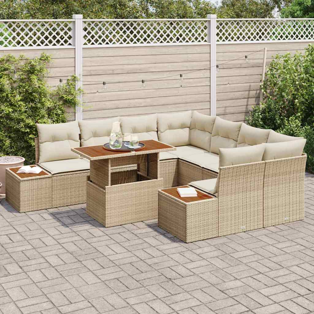 Outdoor-Terrassenset mit beigefarbenen Kissen. Ein Holztisch hat eine Glasflasche und Gläser. Dahinter befindet sich ein weißer Gitterzaun und Grün.