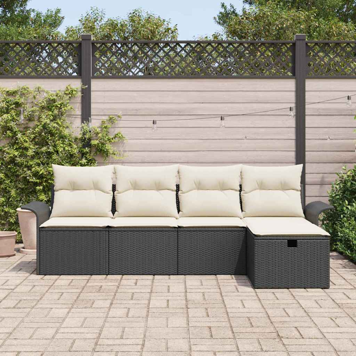 Outdoor-Ecksofa mit cremefarbenen Kissen. Dunkelgraue Korbbasis auf einer Steinterrasse. Holzzaun im Hintergrund.