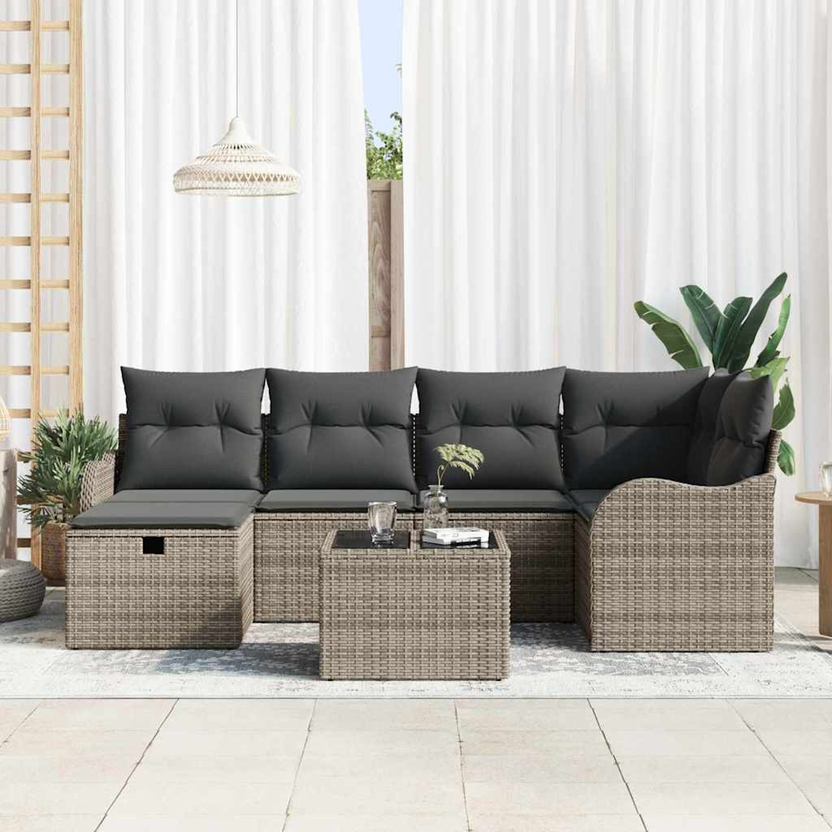 Garten-Sitzgruppe mit grauen Kissen und einem kleinen Tisch. Weiße Vorhänge und Pflanzen im Hintergrund.