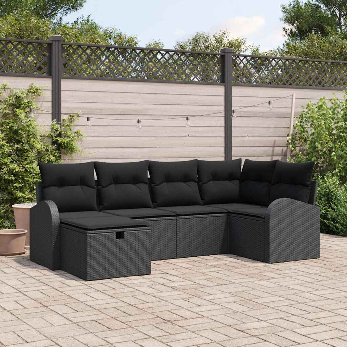 Schwarzes Outdoor-Ecksofa mit schwarzen Kissen auf einer Ziegelterrasse. Ein Holzzaun und Grün bilden den Hintergrund.