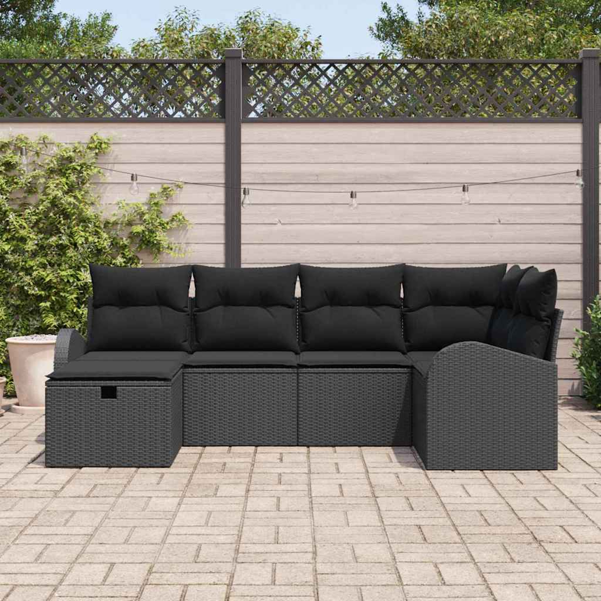 Outdoor-Ecksofa mit schwarzen Kissen. Auf einer Terrasse mit Holzzaun im Hintergrund und Lichterketten.