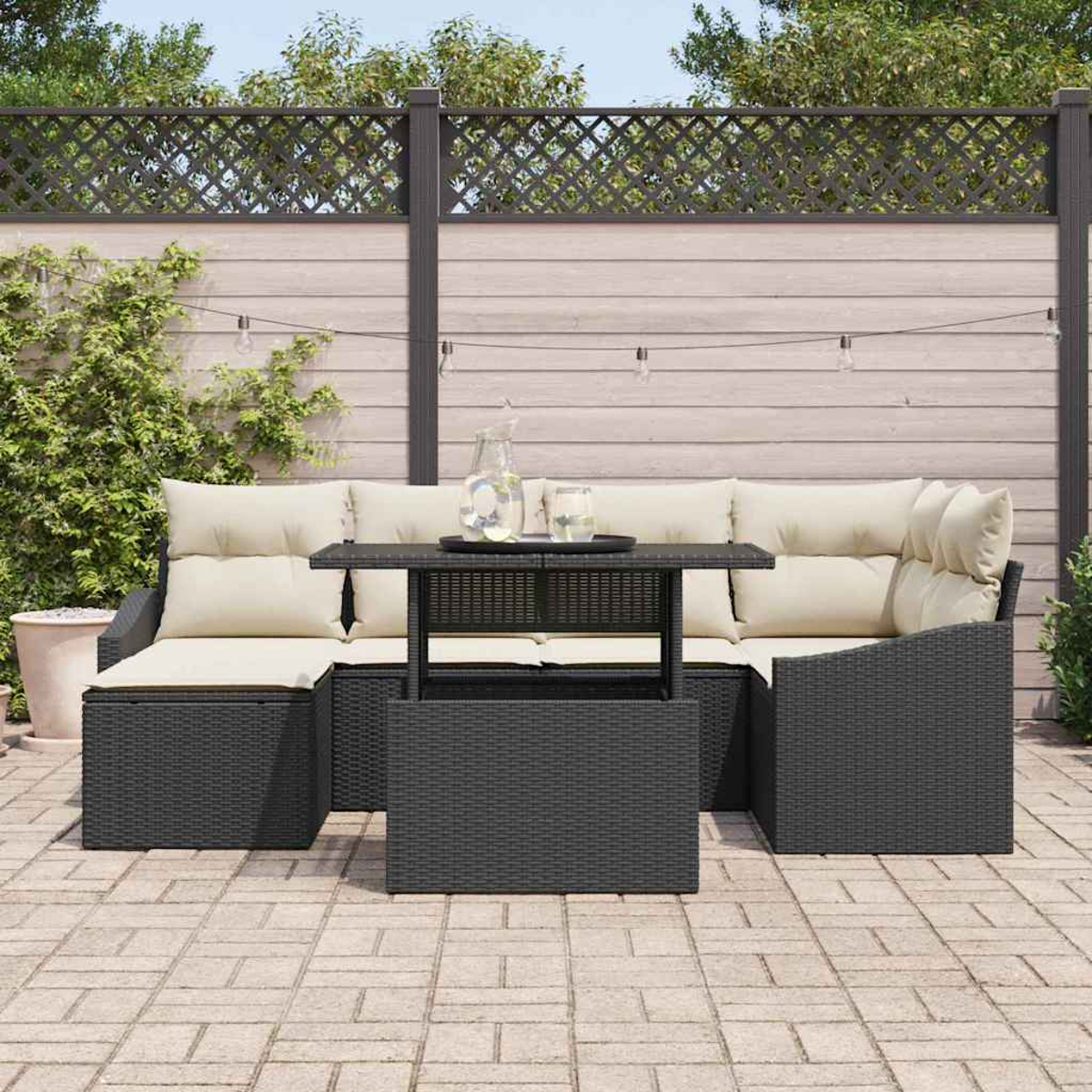 Garten-Sitzgruppe mit beigefarbenen Kissen und einem dunklen Tisch. Im Hintergrund ein Zaun, Pflanzen und Lichterketten.