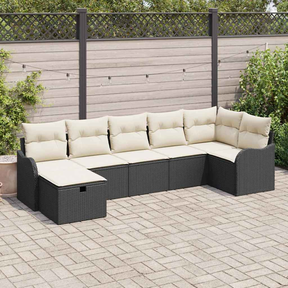 Ein dunkelgraues Outdoor-Ecksofa mit cremefarbenen Kissen steht auf einer Ziegelterrasse. Im Hintergrund sind ein Holzzaun und Pflanzen zu sehen.