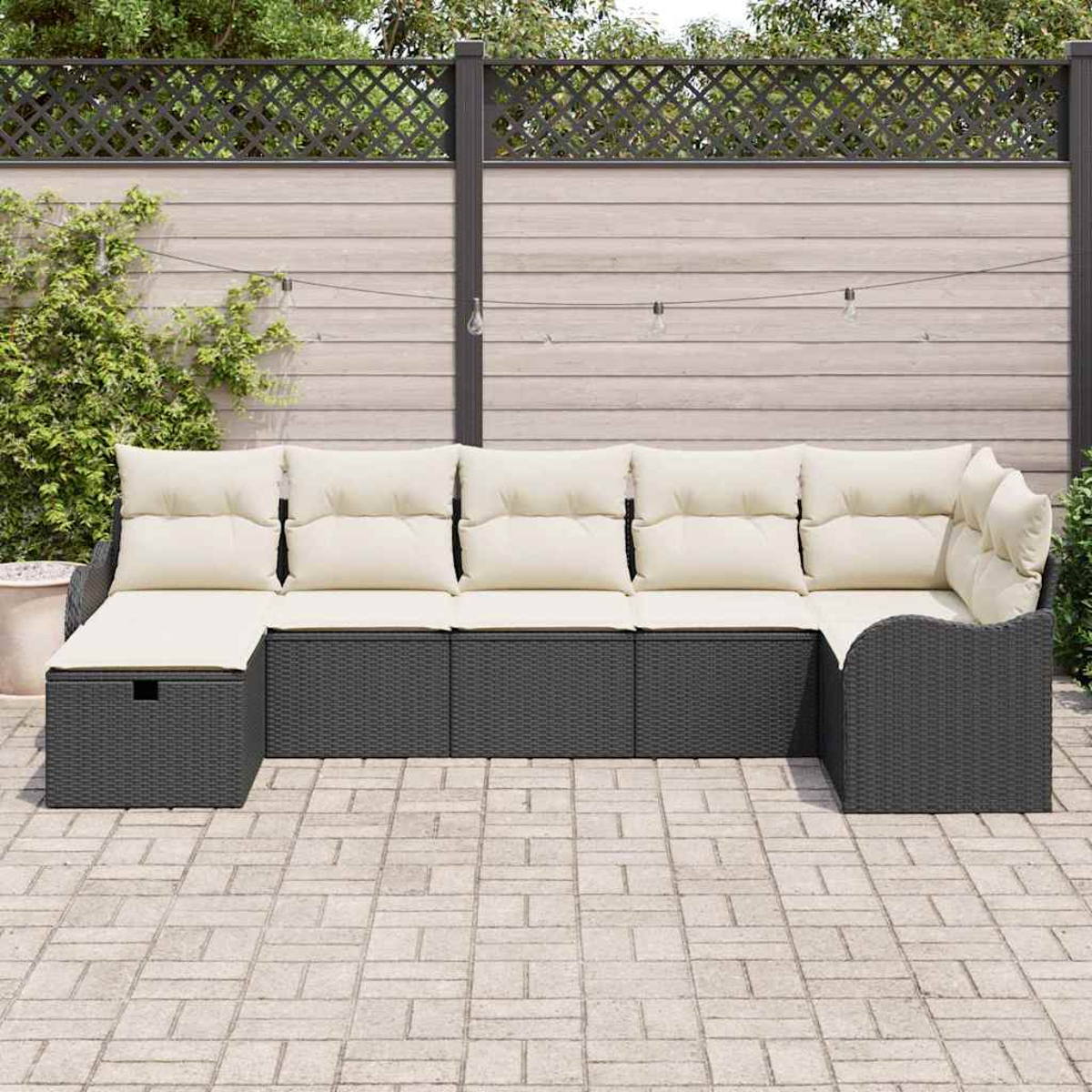 Outdoor-Ecksofa mit cremefarbenen Kissen auf grauem Korbgeflecht, auf einer Ziegelpflasterung. Holzzaun und Grün im Hintergrund.