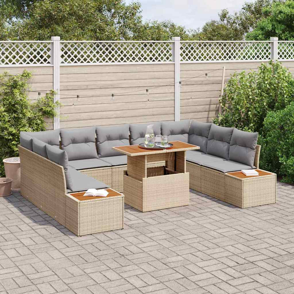 Outdoor-Sofa aus Korbgeflecht mit grauen Kissen und einem Holztisch. Auf einer Terrasse, mit Zaun und Grün im Hintergrund.