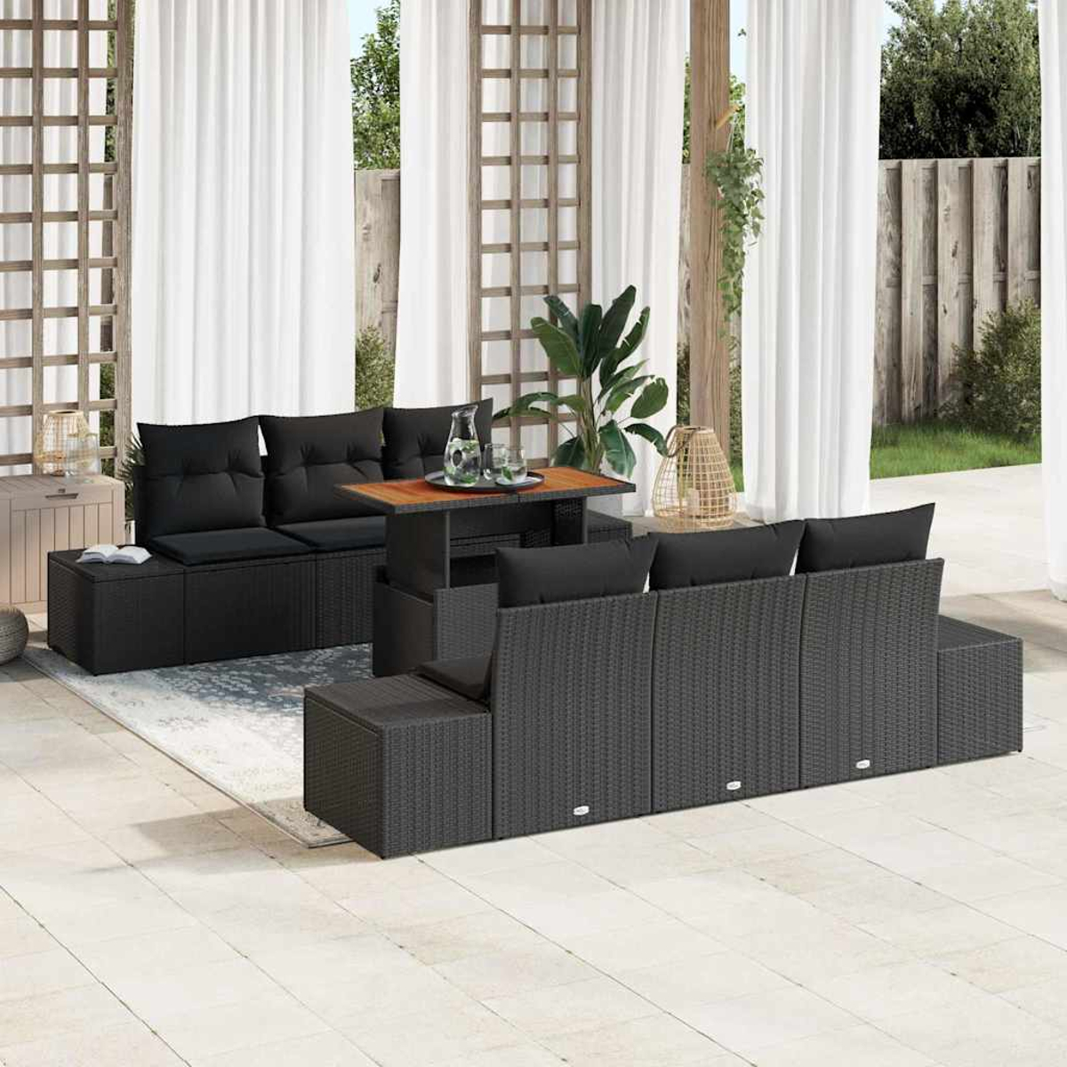 Terrassenmöbel-Set mit schwarzem Korbmöbel, einem Holztisch und weißen Vorhängen. Grüne Pflanzen und ein neutraler Teppich vervollständigen die Szene.