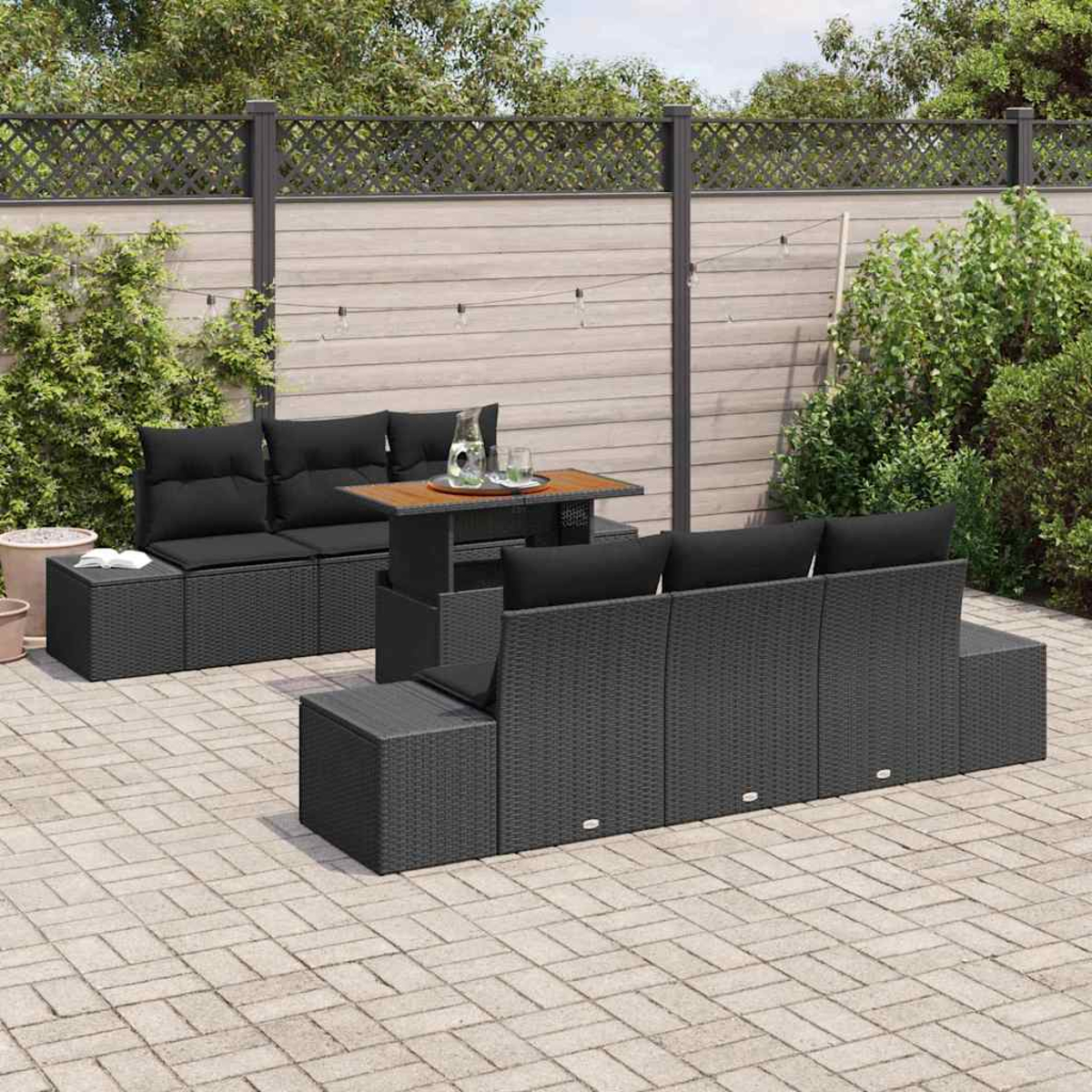 Garten-Sitzgruppe mit schwarzen Kissen und einem Holztisch. Das Set steht auf einer Ziegelstein-Terrasse mit Holzzaun und Grün im Hintergrund.