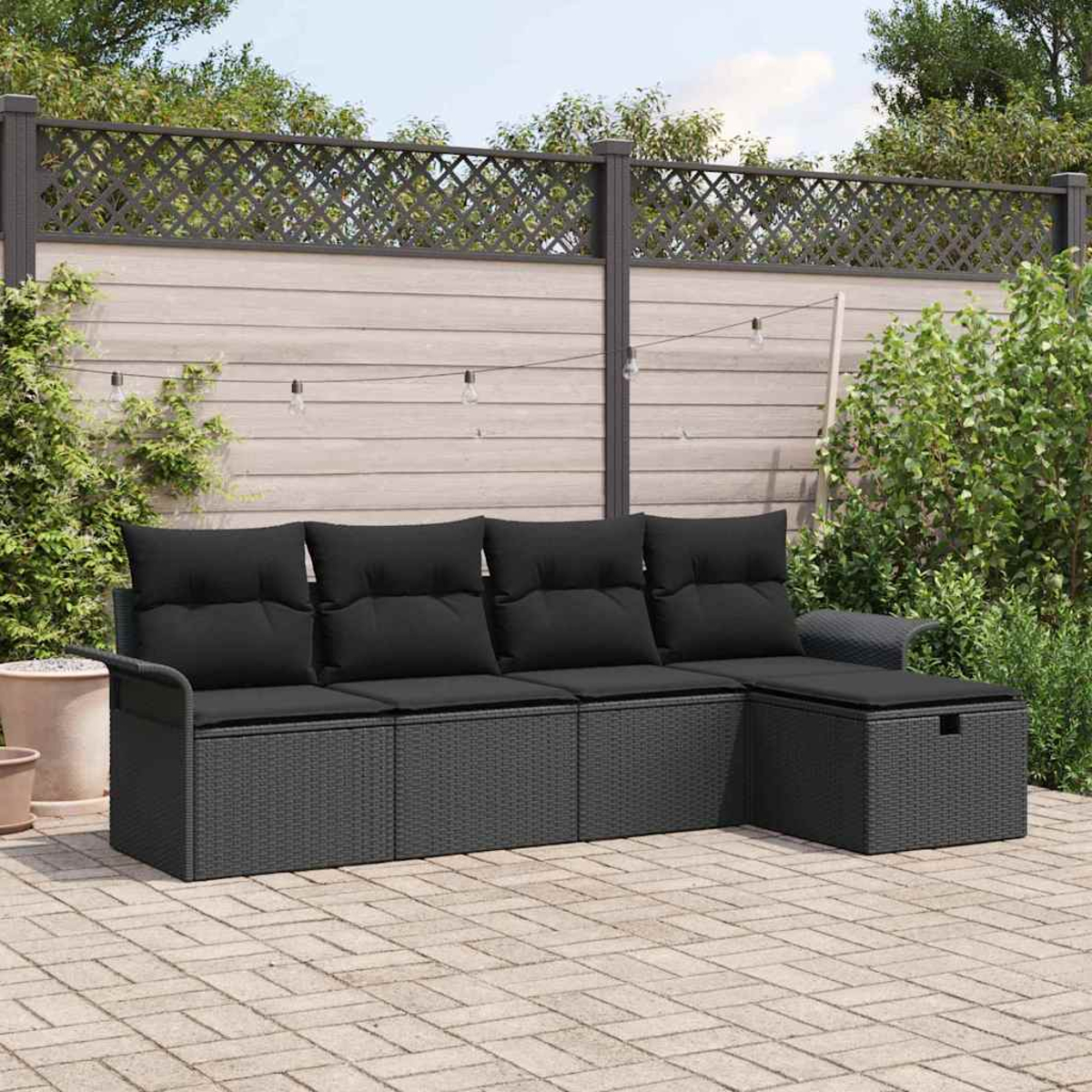 Ein schwarzes Outdoor-Sofa aus Korbgeflecht mit Kissen steht auf einer Terrasse. Im Hintergrund sind ein Zaun mit Pflanzen und Bäumen.