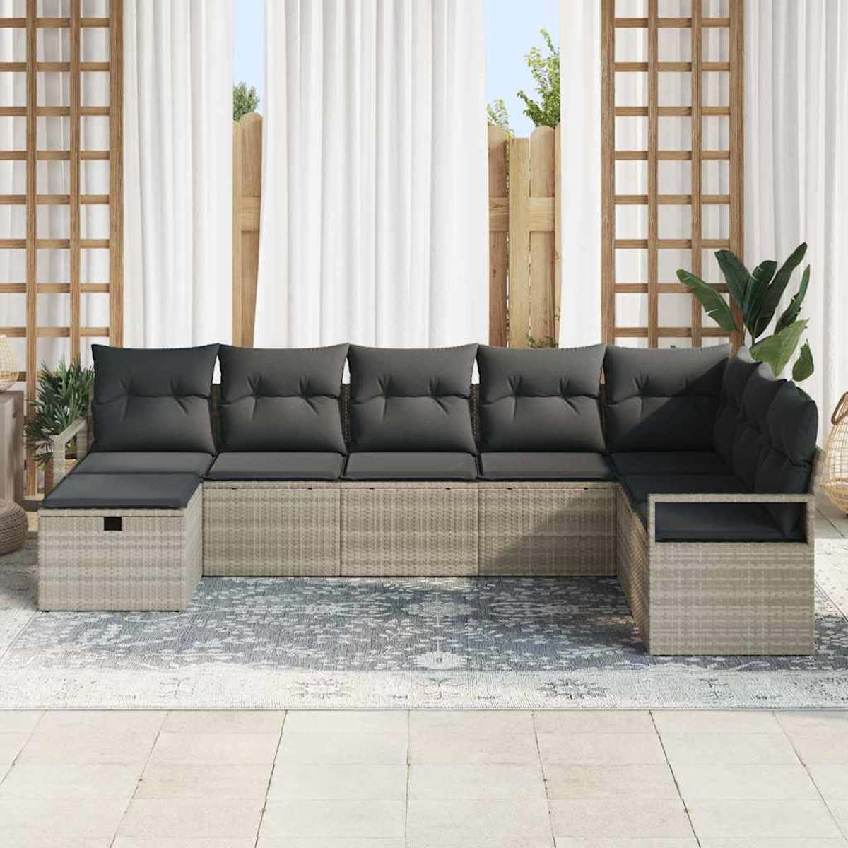 Ein Ecksofa im Freien mit grauen Kissen steht auf einem gemusterten Teppich. Weiße Vorhänge und ein Holzgitter sind im Hintergrund.