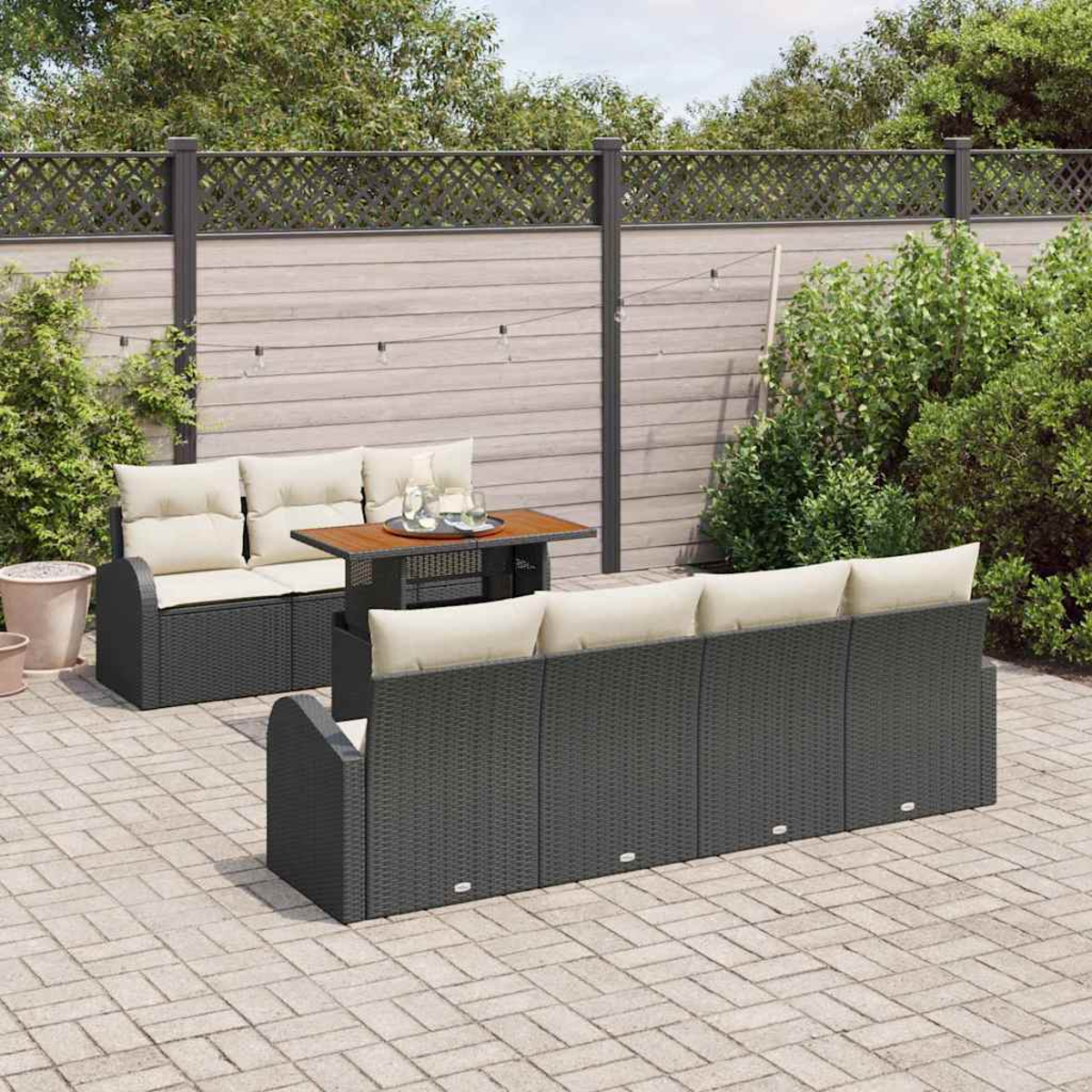 Terrassenset mit schwarzem Korbmöbel, beigen Kissen und einem kleinen Tisch auf einer Steinterrasse, umgeben von Grün.