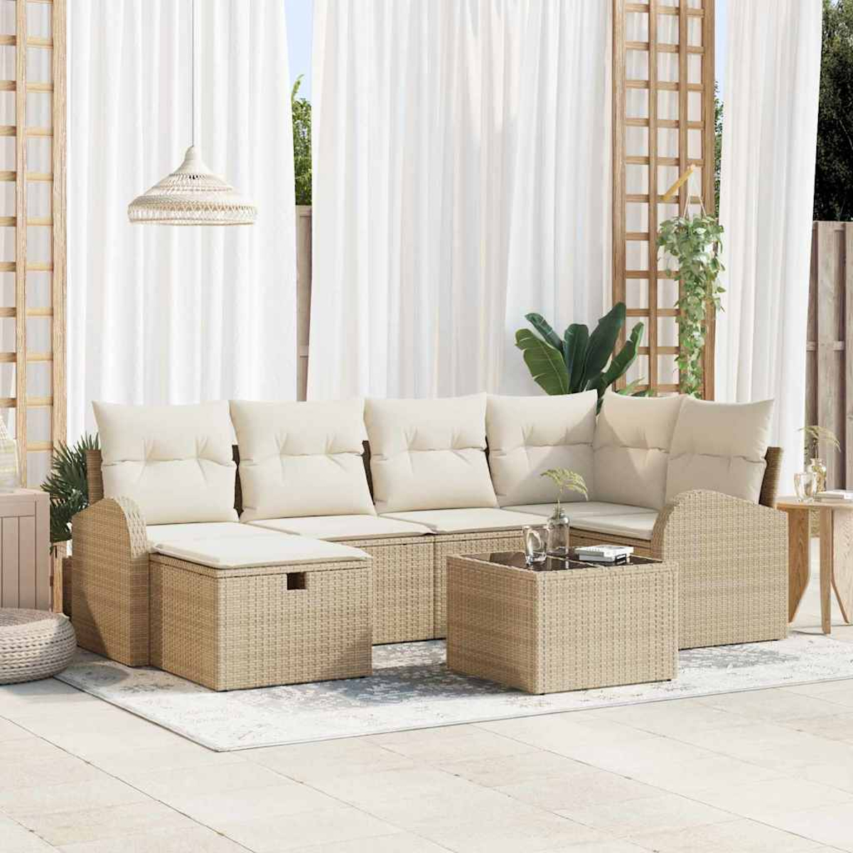 Garten-Korbmöbel-Set mit cremefarbenen Kissen. Beinhaltet Sofa, Ottomane und Couchtisch. Weiße Vorhänge und Pflanzen im Hintergrund.