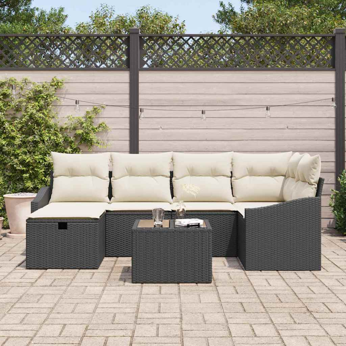 Garten-Sitzgruppe mit dunkelgrauem Korbsessel und Tisch. Beige Kissen, eine Pflanze und ein Zaun im Hintergrund. Lichterkette.