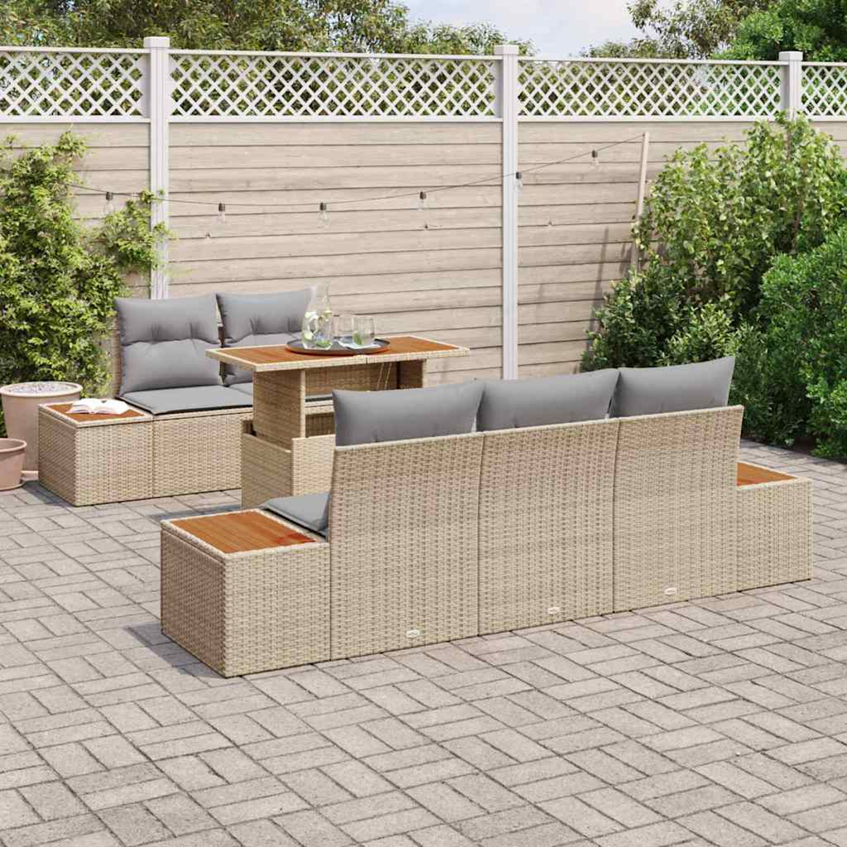 Juego de patio al aire libre con muebles de mimbre beige, cojines grises y una mesa de madera. Una cerca blanca y vegetación al fondo.