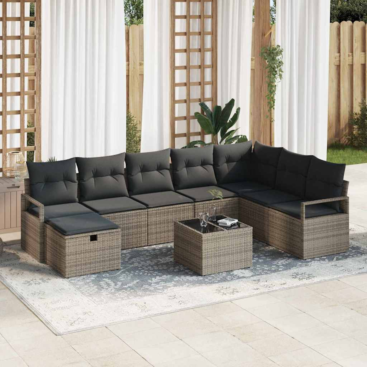 Outdoor-Ecksofa mit grauen Kissen und einem kleinen Tisch auf einem gemusterten Teppich. Weiße Vorhänge und Holzstrukturen im Hintergrund.