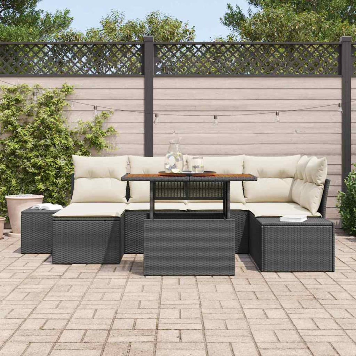Gartensektionssofa mit Tisch, Kissen und Zaun im Hintergrund. Auf dem Tisch stehen ein Krug und Gläser.