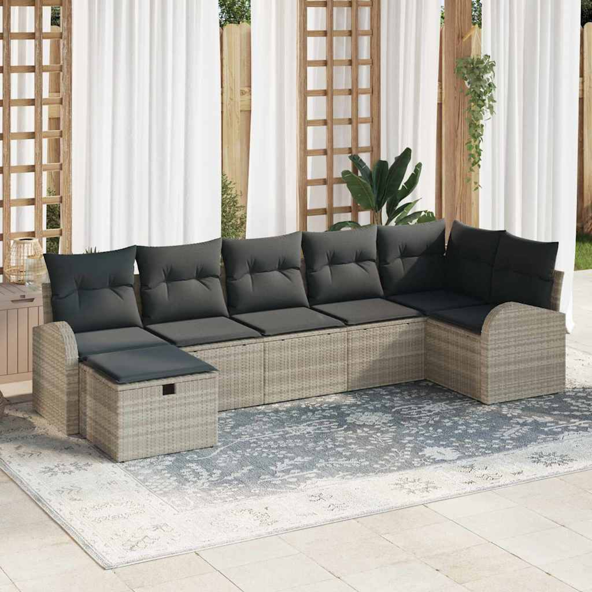 Gartensofa mit grauen Kissen auf einem gemusterten Teppich. Weiße Vorhänge und Holzgitter im Hintergrund.