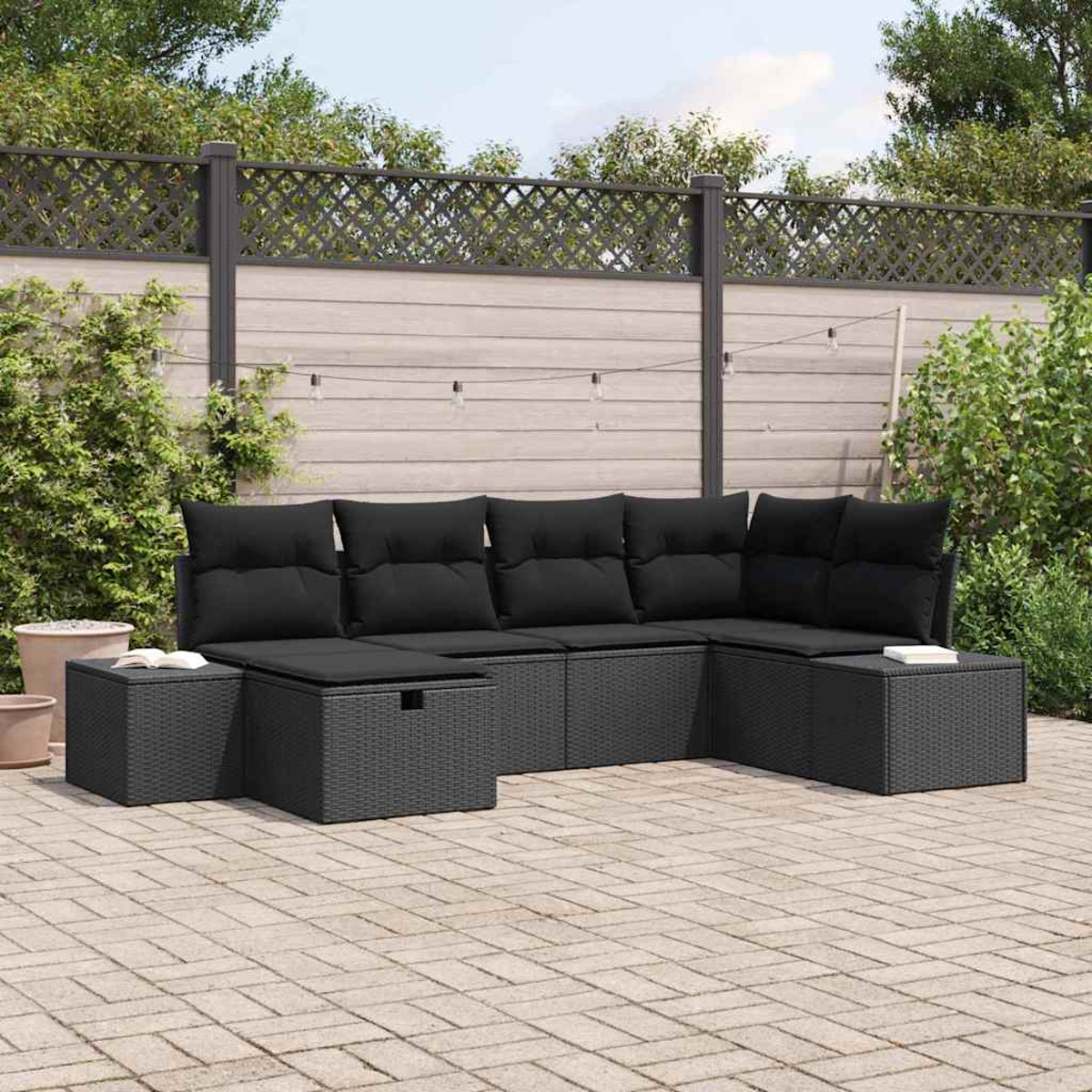 Juego de muebles de mimbre negro para exteriores en un patio. Incluye un sofá seccional, dos otomanas y una valla al fondo.