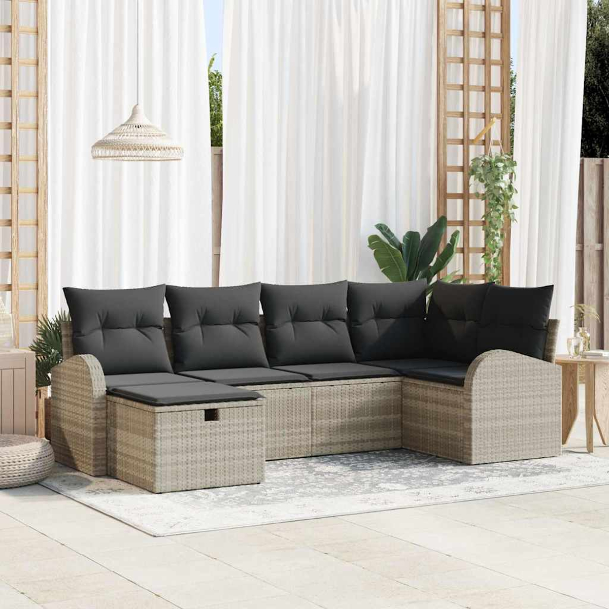 Ein Sitzbereich im Freien mit Korbmöbeln, grauen Kissen, weißen Vorhängen und einem Teppich. Über dem Sofa hängt eine Hängelampe.