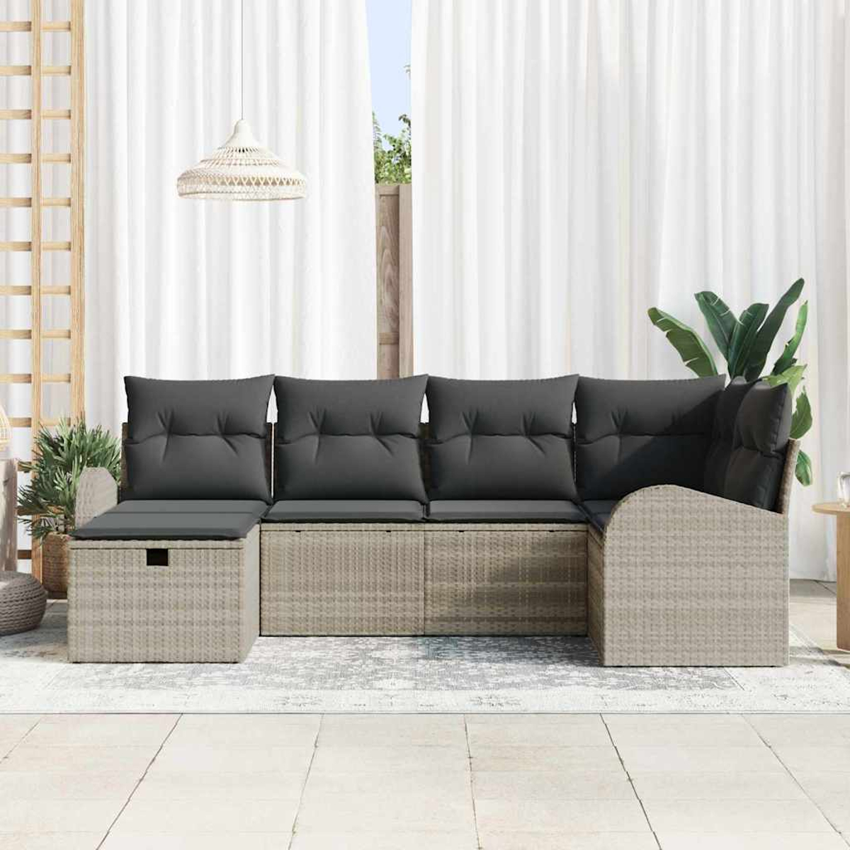 Ein beigefarbenes Outdoor-Ecksofa aus Korbgeflecht mit grauen Kissen steht auf einer Terrasse. Weiße Vorhänge und eine Hängelampe sind im Hintergrund.