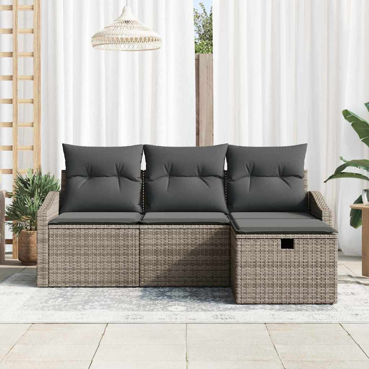 Rattansofa mit grauen Kissen auf einer Terrasse. Weiße Vorhänge im Hintergrund. Eine Hängelampe und Pflanzen sind ebenfalls vorhanden.