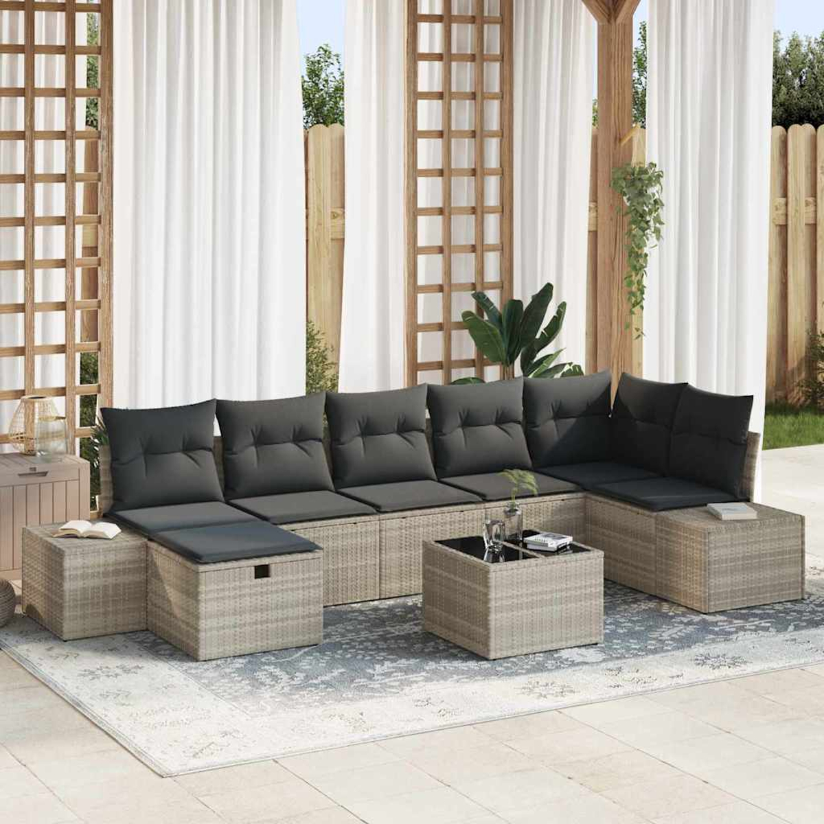 Ein Outdoor-Ecksofa mit grauen Kissen und einem passenden quadratischen Couchtisch steht auf einem gemusterten Teppich in der Nähe weißer Vorhänge.