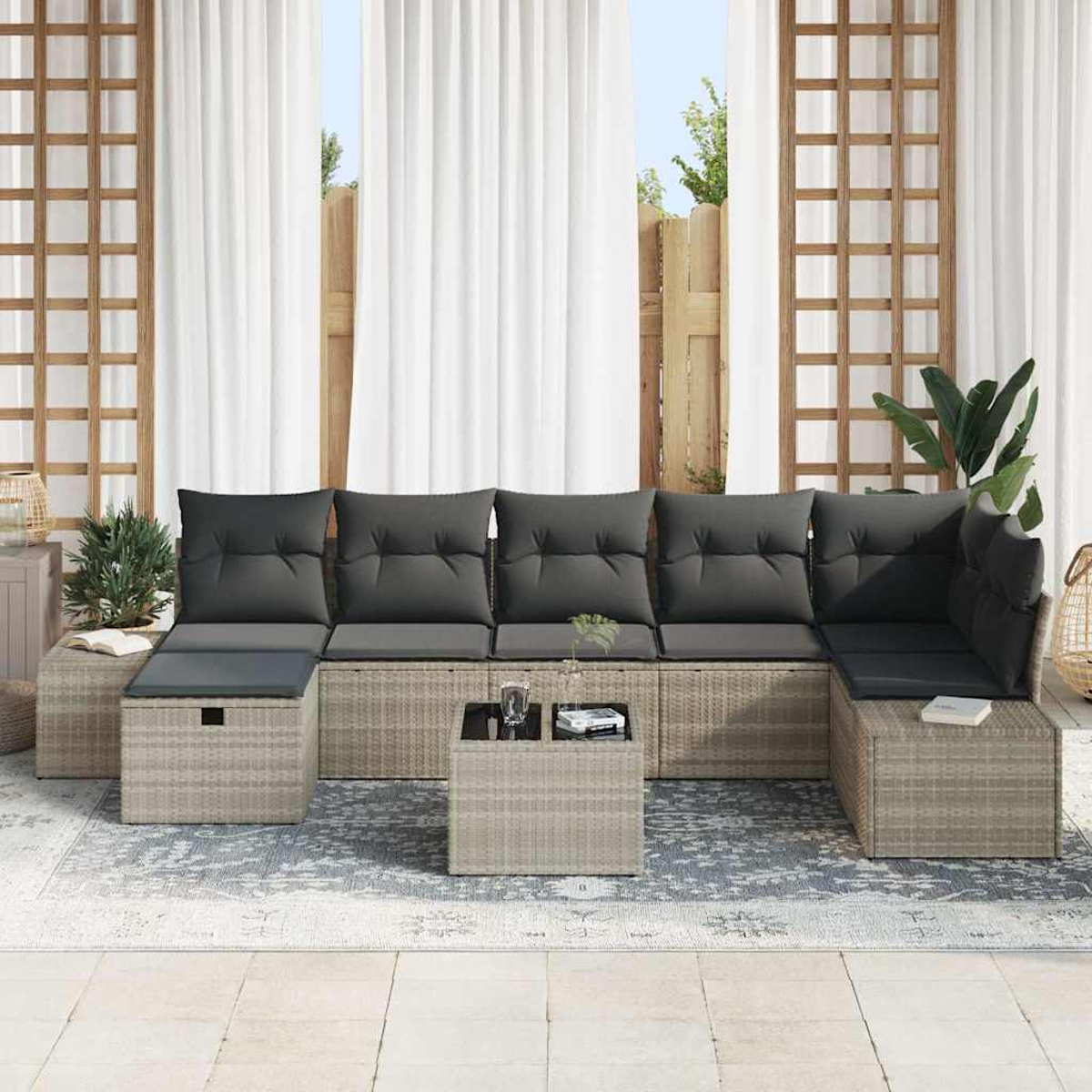 Outdoor-Sofa aus Korbgeflecht mit grauen Kissen. Davor ein kleiner Tisch mit Gläsern und Büchern. Vorhänge und Pflanzen im Hintergrund.
