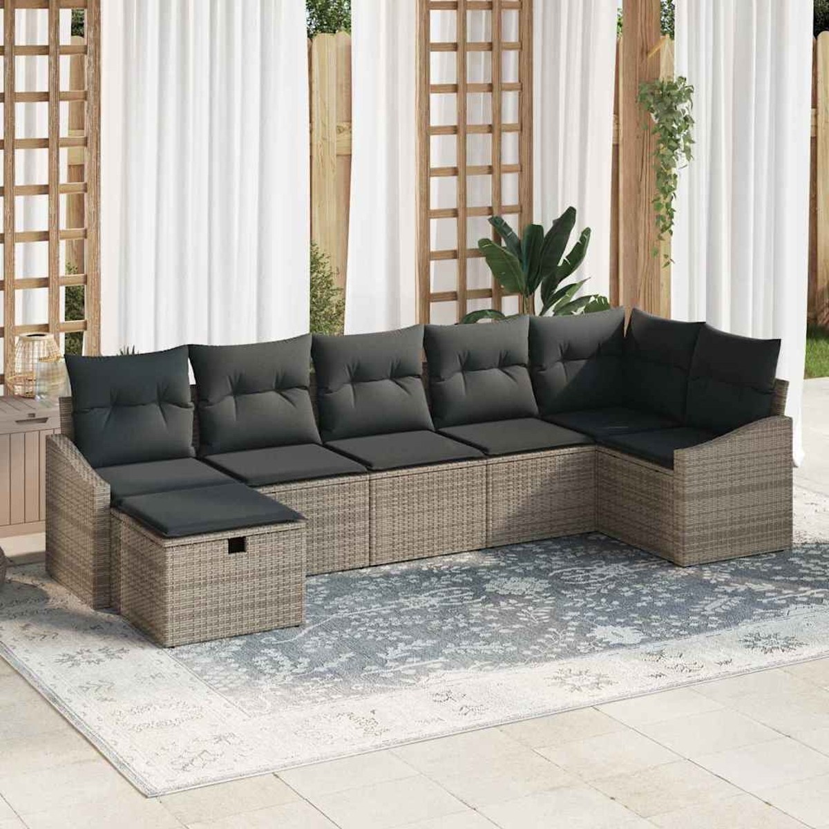Ein Ecksofa aus Korbgeflecht mit schwarzen Kissen steht auf einem Teppich. Weiße Vorhänge und Holzgitter sind im Hintergrund.