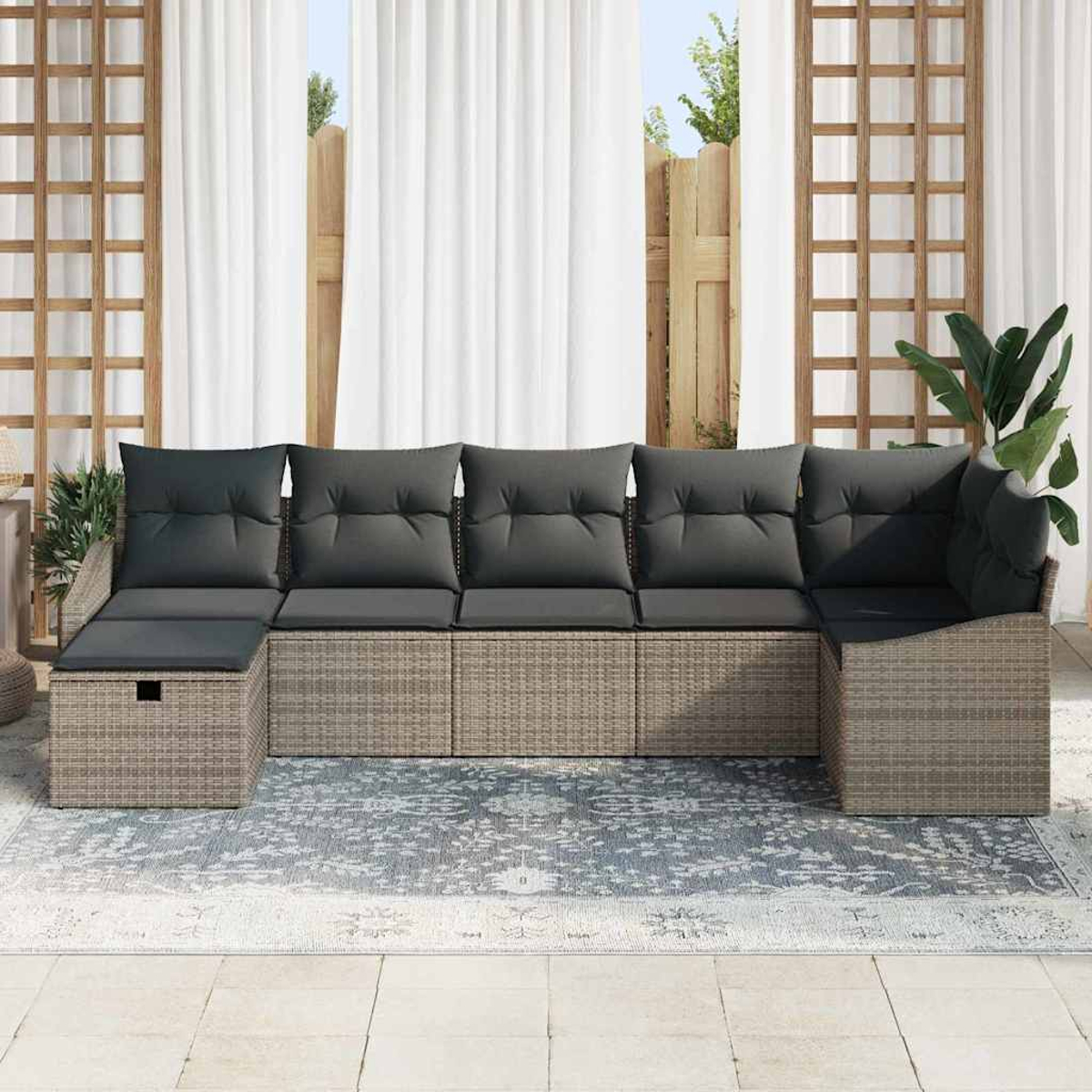 Ein Ecksofa für den Außenbereich mit grauen Kissen steht auf einem gemusterten Teppich. Weiße Vorhänge und ein Holzgitter sind im Hintergrund.