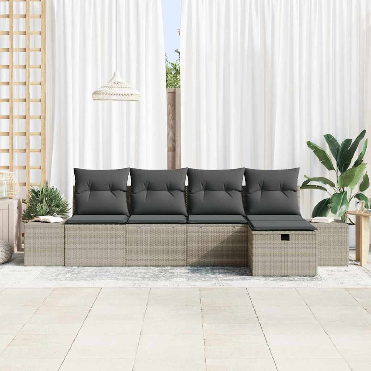 Gartencouch mit grauen Kissen und grauem Rattansockel. Weiße Vorhänge im Hintergrund. Pflanze rechts. Dekoratives Holzpaneel links.