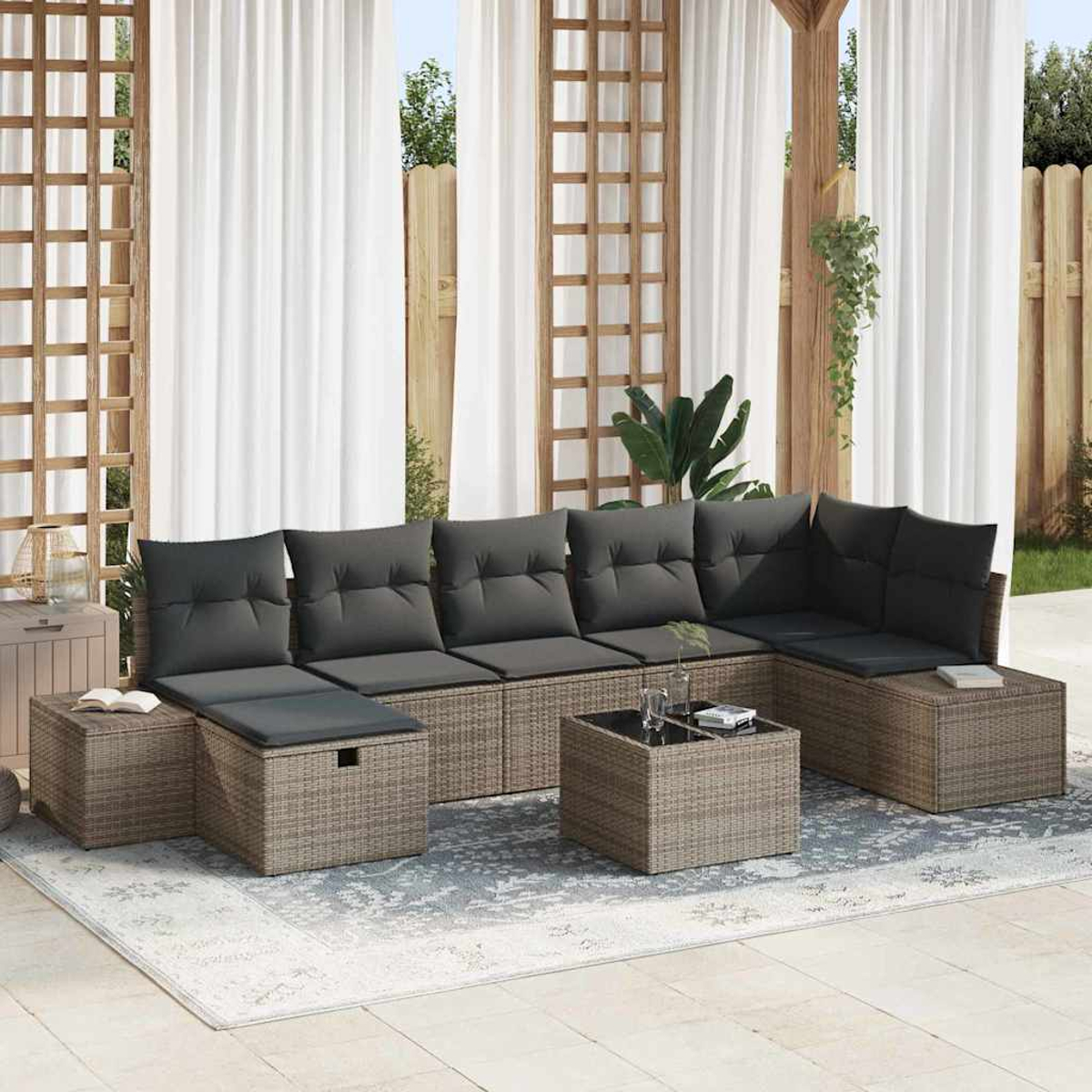 Eine Sitzecke im Freien mit einem Ecksofa im Korbstil, grauen Kissen und einem kleinen Tisch auf einem gemusterten Teppich.