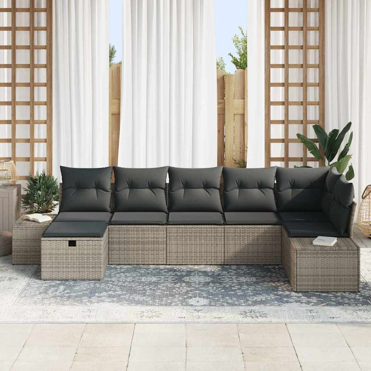 Outdoor-Ecksofa mit grauen Kissen auf einem gemusterten Teppich, in der Nähe von weißen Vorhängen und Holzgittern, Pflanzen im Hintergrund.