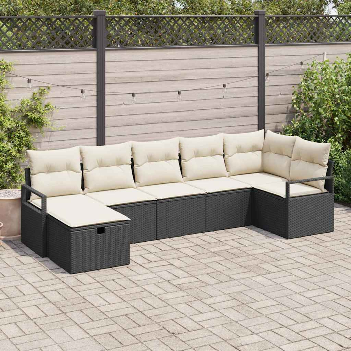 Outdoor-Ecksofa mit beigen Kissen und grauem Rattan. Auf einer Backstein-Terrasse, mit Holzzaun und Grün im Hintergrund.