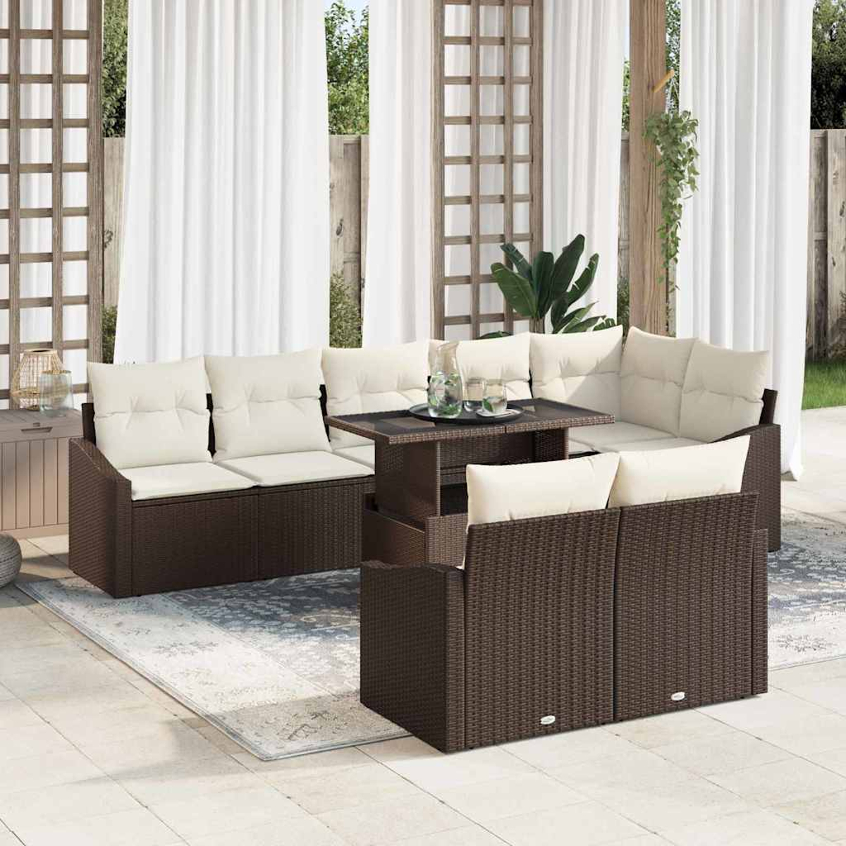 Terrassenmöbel-Set mit braunen Korbmöbeln und cremefarbenen Kissen. Inklusive Couchtisch und Teppich. Weiße Vorhänge im Hintergrund.
