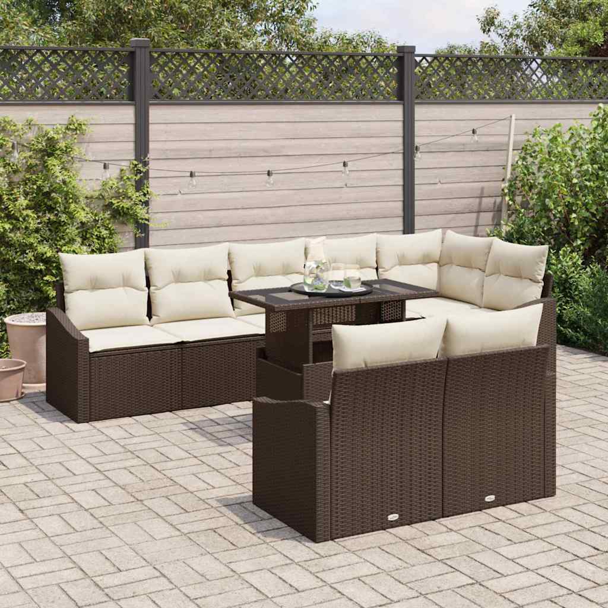 Terrassenmöbel-Set im Freien mit braunen Korbmöbeln, cremefarbenen Kissen und einem Tisch mit Glasplatte. Auf einer Backsteinterrasse, im Hintergrund ein Zaun.