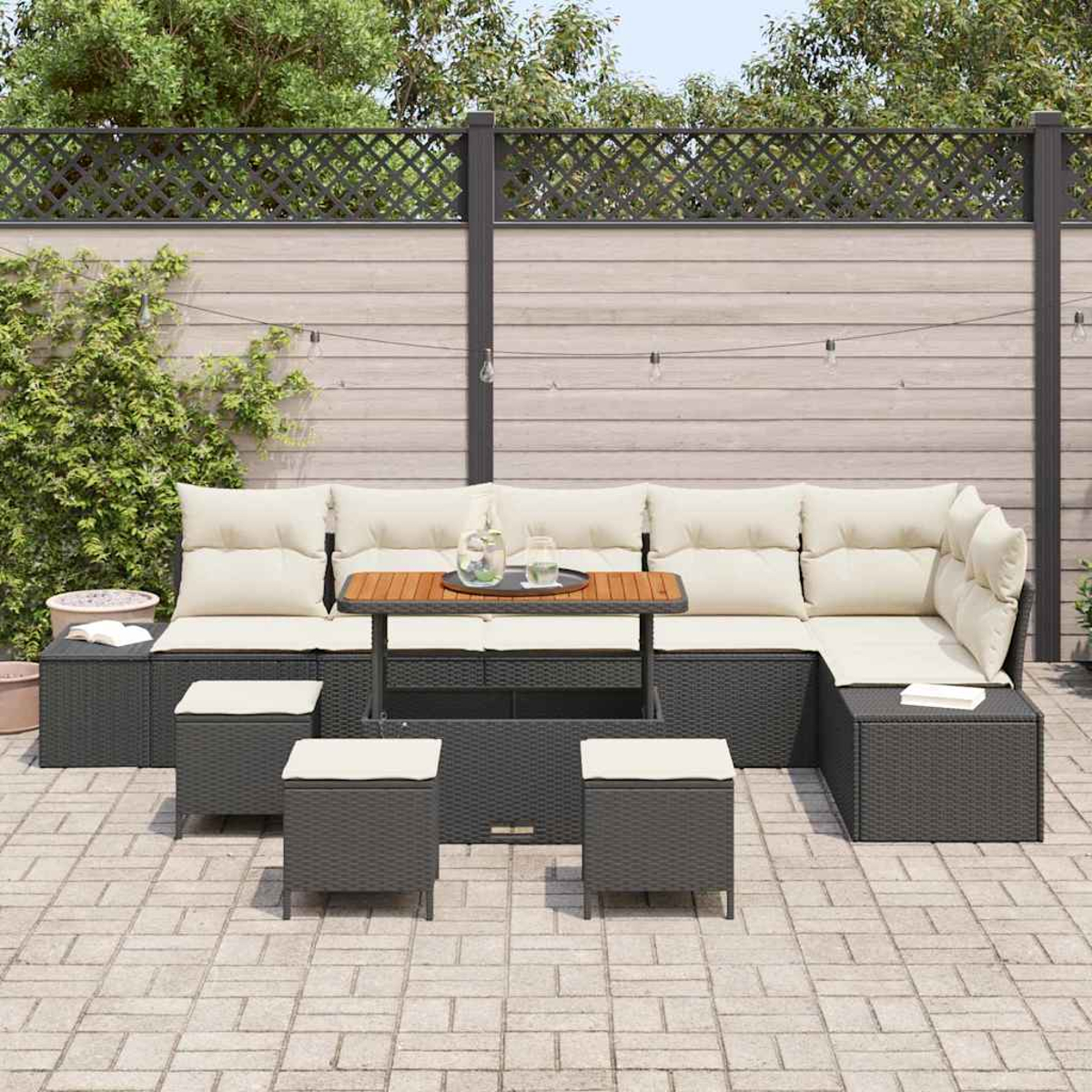 Garten-Lounge-Set mit grauen Korbmöbeln, cremefarbenen Kissen und einem Holztisch. Auf Ziegelpflaster angeordnet, mit Zaun im Hintergrund.