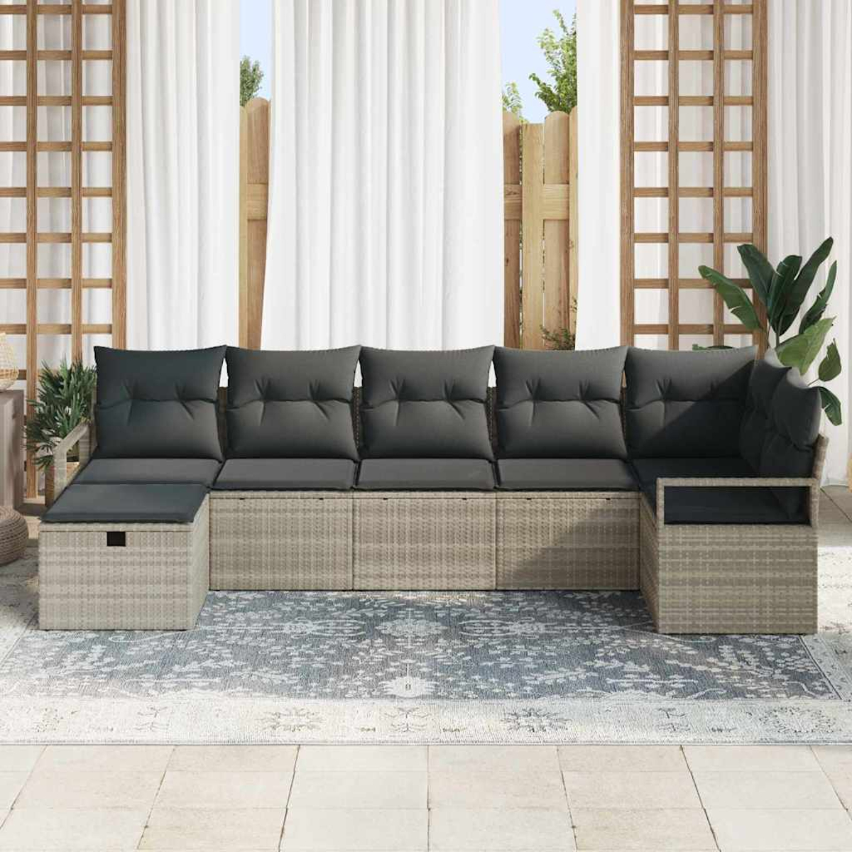 Outdoor-Ecksofa mit grauen Kissen auf einem gemusterten Teppich. Weiße Vorhänge und Holzgitter im Hintergrund.