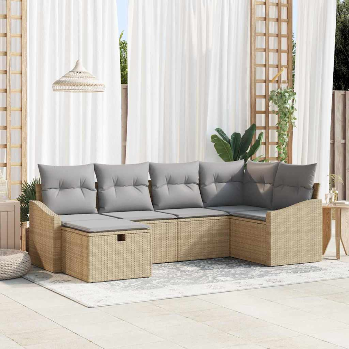 Geflochtenes Ecksofa mit grauen Kissen auf einer Terrasse. Weiße Vorhänge im Hintergrund. Pflanze und Holzgitter rechts.